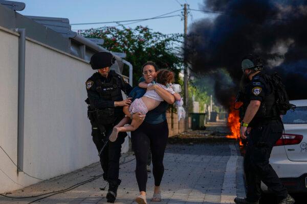 Israeli police officers evacuate a woman and a child from a site hit by a rocket that was fired from the Gaza Strip, in Ashkelon, Israel, on Oct. 7, 2023. (AP Photo/Tsafrir Abayov)