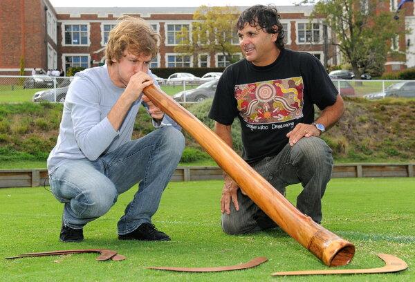 Red Bull Racing Formula One driver Sebastian Vettel of Germany is given lessons on how to play a didgeridoo, an Aboriginal musical instrument, by Indigenous Cultural Awareness Facilitator, Ron Murray, on March 24, 2010. (William West/AFP via Getty Images)