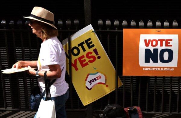 A woman handing out brochures walks past referendum promotional posters outside a voting centre in central Sydney, Australia, on Oct. 3, 2023. (David Gray/AFP via Getty Images)