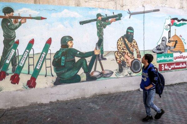 A child walks past a mural depicting soldiers firing rockets as Palestinians mark the 34th anniversary of the founding of the Islamist Hamas movement, which rules the Palestinian strip, on December 11, 2021. (Said Khatib/AFP via Getty Images)