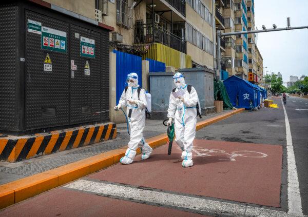 Health workers wear protective clothing as they walk to disinfect an area outside an apartment building under lockdown after a case of COVID-19 in Beijing on May 9, 2022. (Photo by Kevin Frayer/Getty Images)