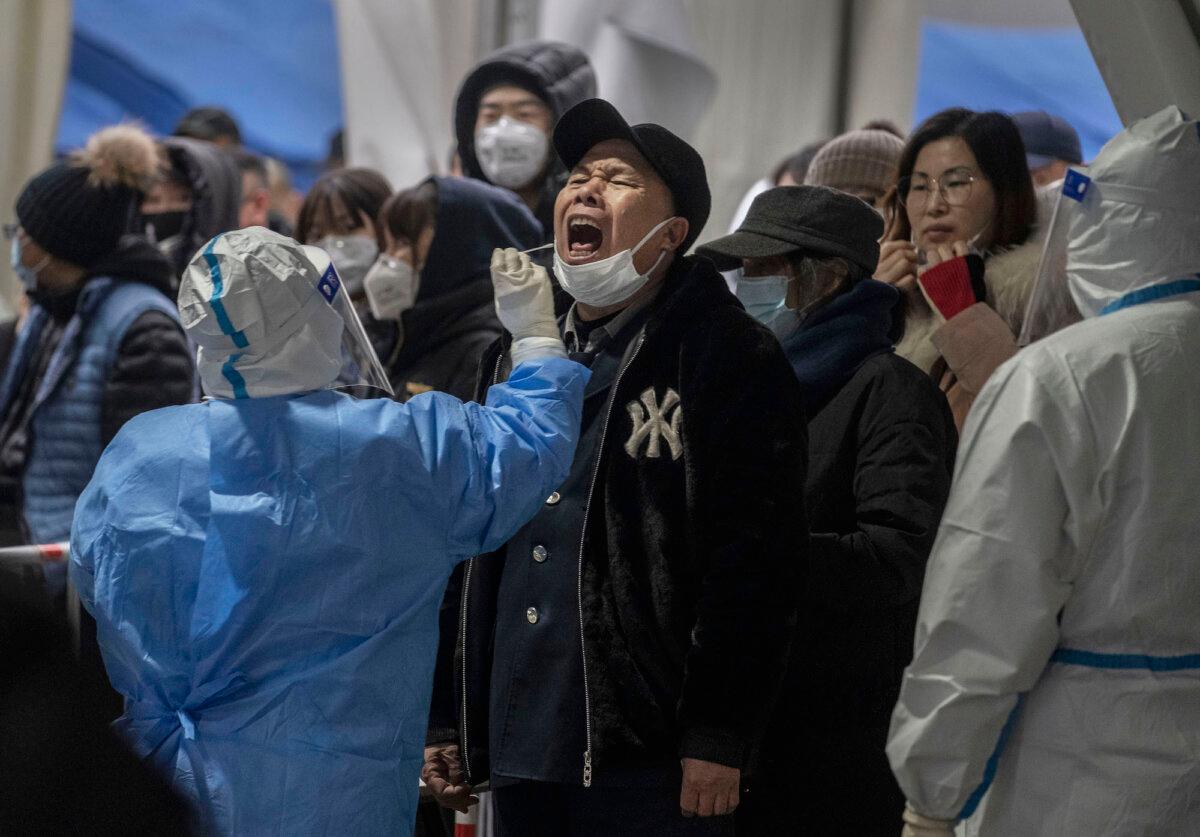 A health worker in protective gear gives a nucleic acid test to detect COVID-19 to a man as others line up at a mass testing site in Beijing on Jan. 24, 2022. (Kevin Frayer/Getty Images)