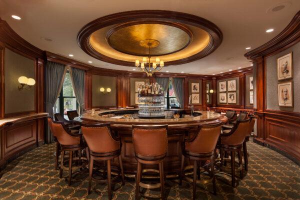 The Round Robin Bar is known for its circular design, oak-paneled walls, button-tufted leather seating, and framed portraits of famed visitors. Considered a meeting place for Washington's political and social elite since 1847, the polished mahogany bar’s design is intended to enhance conversation, and the carved-wood ceiling design proportionally mirrors the bar. (Courtesy of Willard InterContinental Washington)