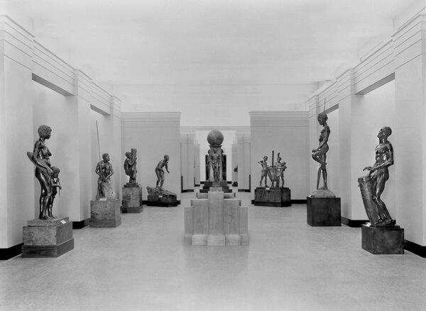 The first gallery of the “Hall of Man” exhibition at the Field Museum in Chicago, in 1933. (L) Statues of an Australian, a Semang Pigmy (Malay Peninsula), a Solomon Islander, and a Hawaiian. (R) Life-size bronze statues of Africans. (C) A heroic sculpture representing the unity of humankind depicting the white, yellow, and black races topped with a terrestrial globe. Heroic sculptures are life-size or larger, denoting the importance of the work. (Field Museum)