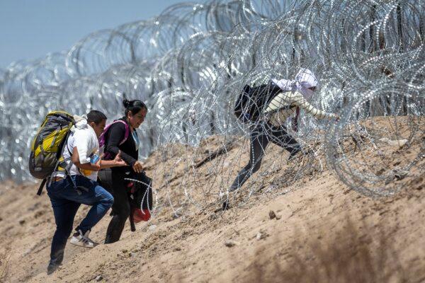 Illegal immigrants walk through razor wire surrounding a makeshift migrant camp after crossing the border from Mexico, in El Paso, Texas, on May 11, 2023. (John Moore/Getty Images)