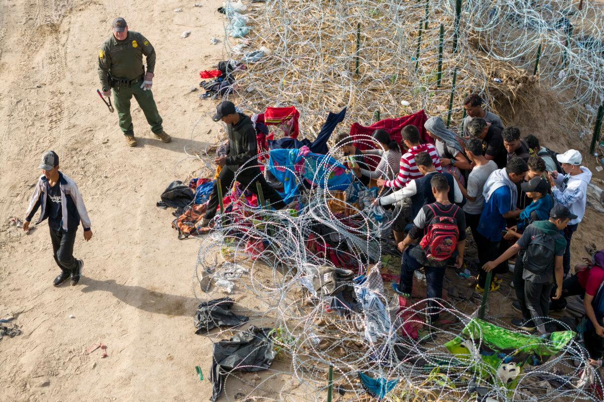 An aerial view shows a U.S. Border Patrol agent supervising as illegal immigrants walk into the United States after crossing the Rio Grande from Mexico on Sept. 30, 2023, in Eagle Pass, Texas. The agent had cut coils of razor wire to let them pass through for processing. (John Moore/Getty Images)