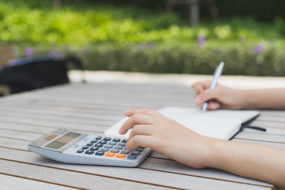 A child budgets carefully using a ledger and calculator. (Illustration - Komkritphoto/Shutterstock)