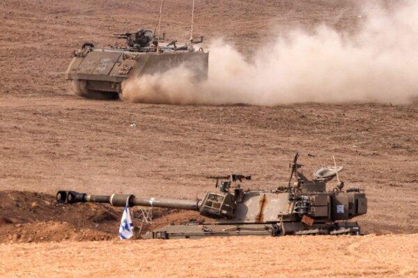 An Israeli army armored tracked vehicle moves near a stationed artillery howitzer at a position along the border with the Gaza Strip in southern Israel on Oct. 31, 2023, amid ongoing battles between Israel and the Palestinian Hamas movement. (Jack Guez/AFP via Getty Images)