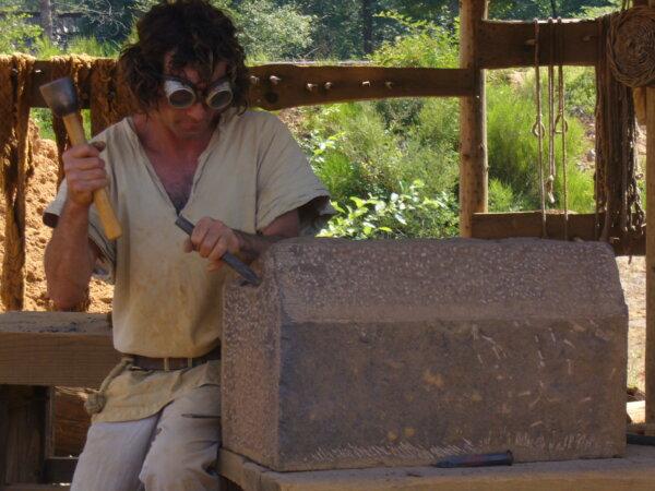 A stone mason hews stone with handmade tools. Goggles are required by the French government for safety. (Copyright Guédelon)