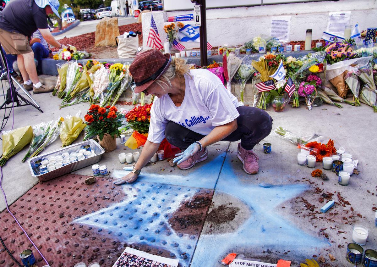 Elena Colombo makes a Star of David out of chalk among flowers and candles left at a makeshift memorial placed at the scene of a Nov. 5 confrontation that led to the death of a demonstrator in Thousand Oaks, Calif., on Nov. 7, 2023. (AP Photo/Richard Vogel)