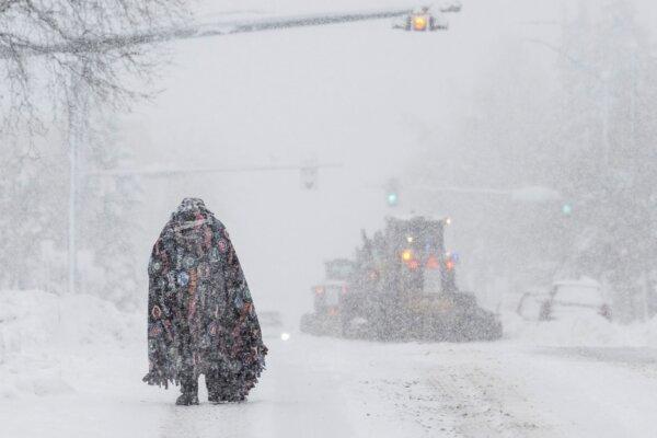 A pedestrian takes cover under a blanket on Cordova Street as plows clear the roadway, in Anchorage, Alaska on Nov. 9, 2023. (Marc Lester/Anchorage Daily News via AP)
