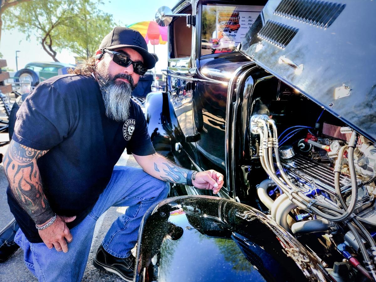 Rocky Stroh of Casa Grande, Ariz., kneels beside the 1931 Ford Model A that he and his father rebuilt from scratch. Photo taken on Nov. 4, 2023. (Allan Stein/The Epoch Times)