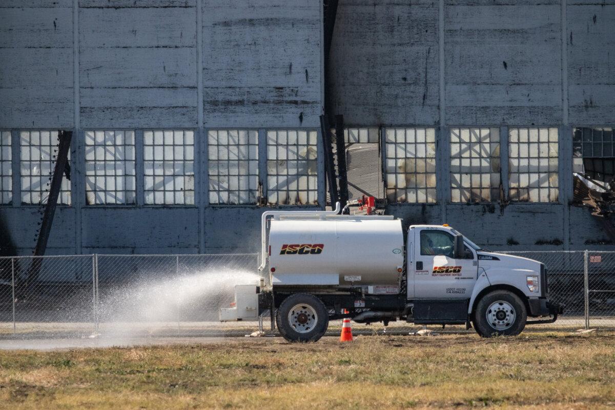 A water truck soaks the ground as a fire continues to burn in a historic blimp hangar in Tustin, Calif., on Nov. 14, 2023. (John Fredricks/The Epoch Times)