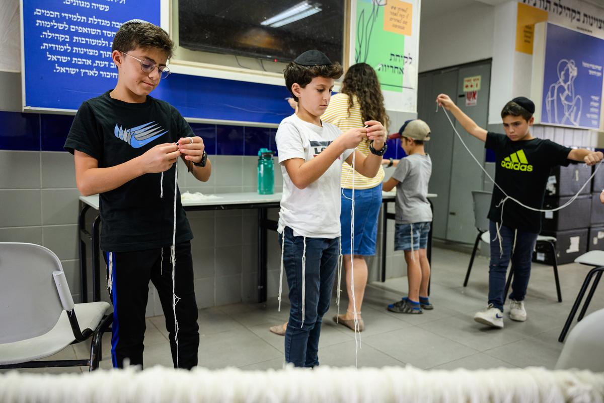 Benjamin (C), aged 10, teaches other boys how to make tzitzis, a type of traditional religious fringe, which will be attached to garments worn by members of the IDF, at a girl's high school in Beit Shemesh, Israel, on Oct. 16, 2023. (Leon Neal/Getty Images)