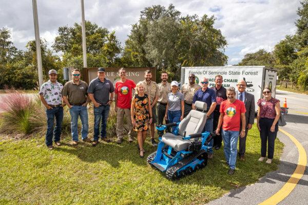 Central Florida volunteers, supporters and park rangers including George Koutsakis, president of Friends of Seminole State Forest, fourth from left, Katherine Hallum of Friends of Blue Spring, fifth from left, Blue Spring State Park rangers, state Rep. Rachel Plakon, middle, and Greg Pauch of the Mesara Family Foundation, fifth from right, gather at Blue Spring State Park in Orange City, Florida, to celebrate a new tracked chair program for visitors with mobility impairments on Oct. 26, 2023. (Patrick Connolly/Orlando Sentinel/TNS)