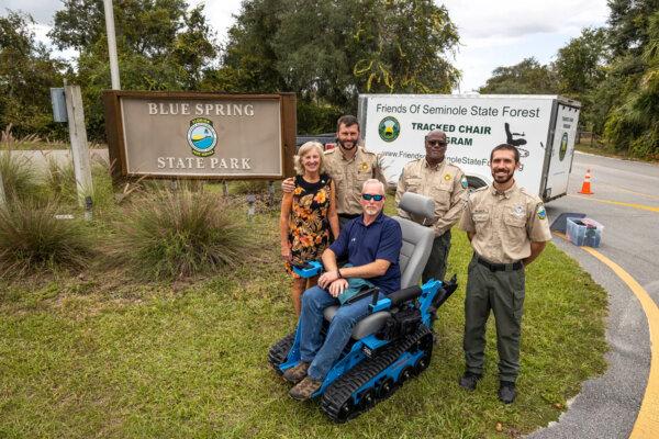 At the entrance of Blue Spring State Park in Orange City, Florida, from left, Katherine Hallum of Friends of Blue Spring; Dustin Allen, park manager; Greg Pauch of the Mesara Family Foundation; Darrell Thomas, assistant park manager; and Connor Wagner, park services specialist, gather to celebrate a new tracked chair program for visitors with mobility impairments on Oct. 26, 2023. The chairs can be reserved free of charge through an online system. (Patrick Connolly/Orlando Sentinel/TNS)