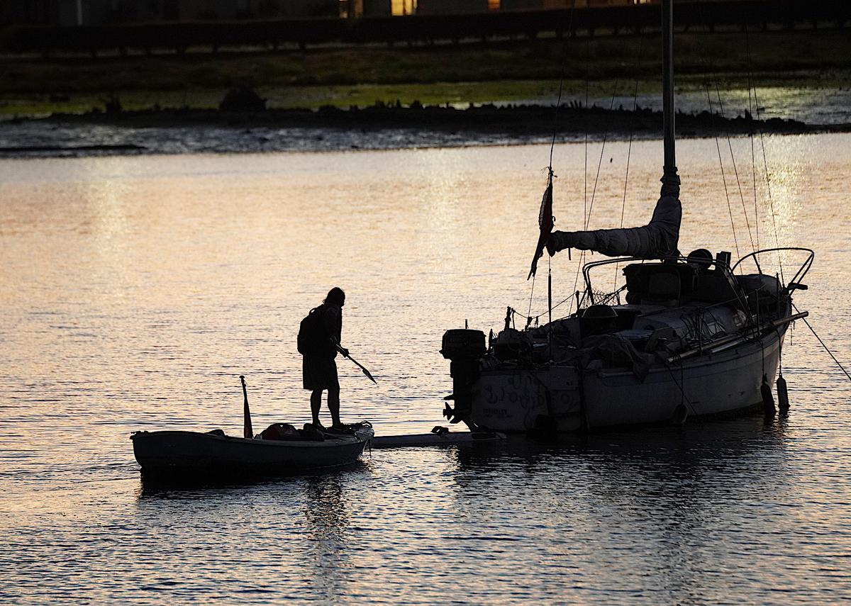  A homeless man brings his small boat alongside a derelict vessel anchored illegally in the Oakland Estuary on Nov. 13, 2023. (Allan Stein/The Epoch Times)