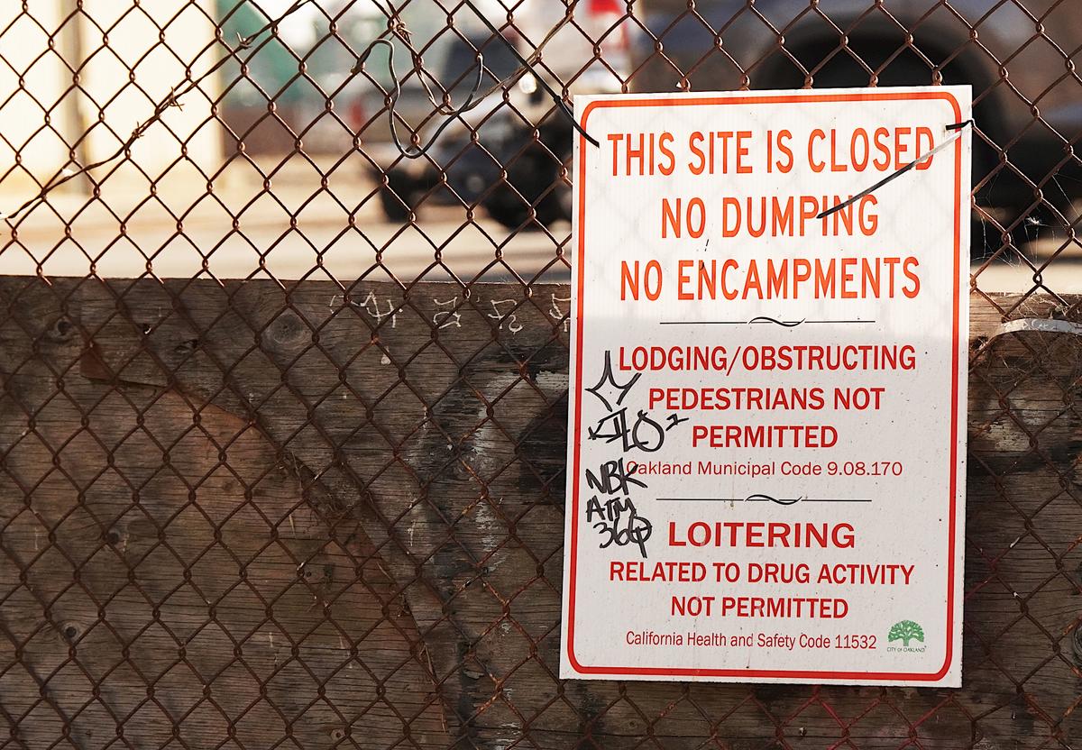 A sign on a fence from the Oakland municipal government instructs people not to camp, dump trash, or loiter. Robberies in Oakland have increased by 20 percent this year, according to the city's police department. (Allan Stein/The Epoch Times)