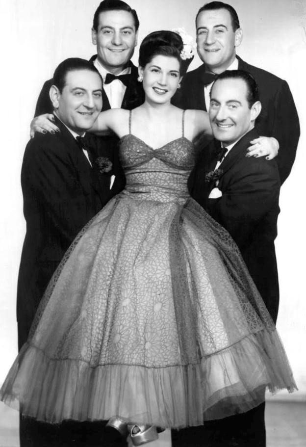Guy Lombardo and his siblings on CBS Radio’s Three Ring Time program, circa 1954. Clockwise from top left: Guy, Victor, Lebert, and Carmen, with Rose Marie in the center. (Public Domain)