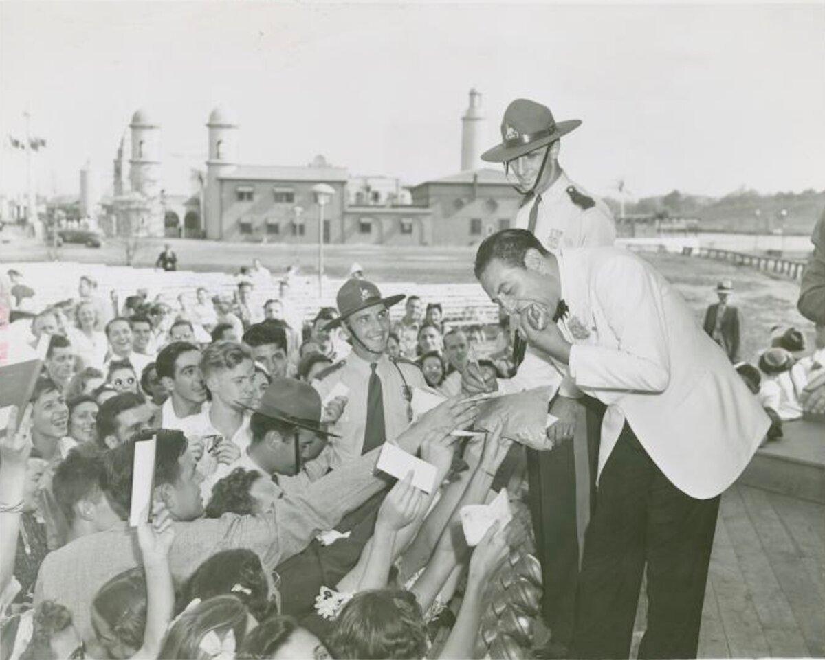 Guy Lombardo eats a hot dog and signs autographs for fans, circa 1935 to 1945. (Public Domain)