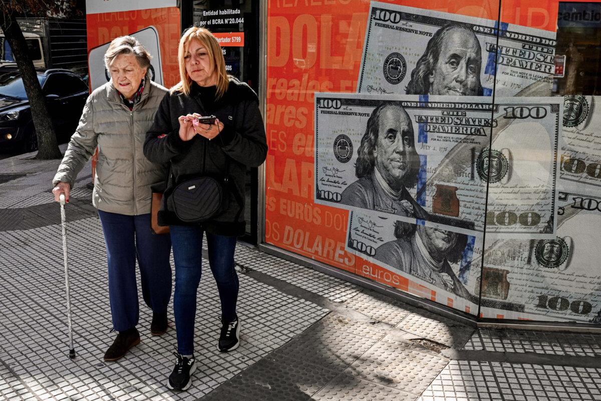 Women walk past an image of $100 notes in Buenos Aires on Aug. 14, 2023, a day after primary elections in Argentina. (Luis Robayo/AFP via Getty Images)