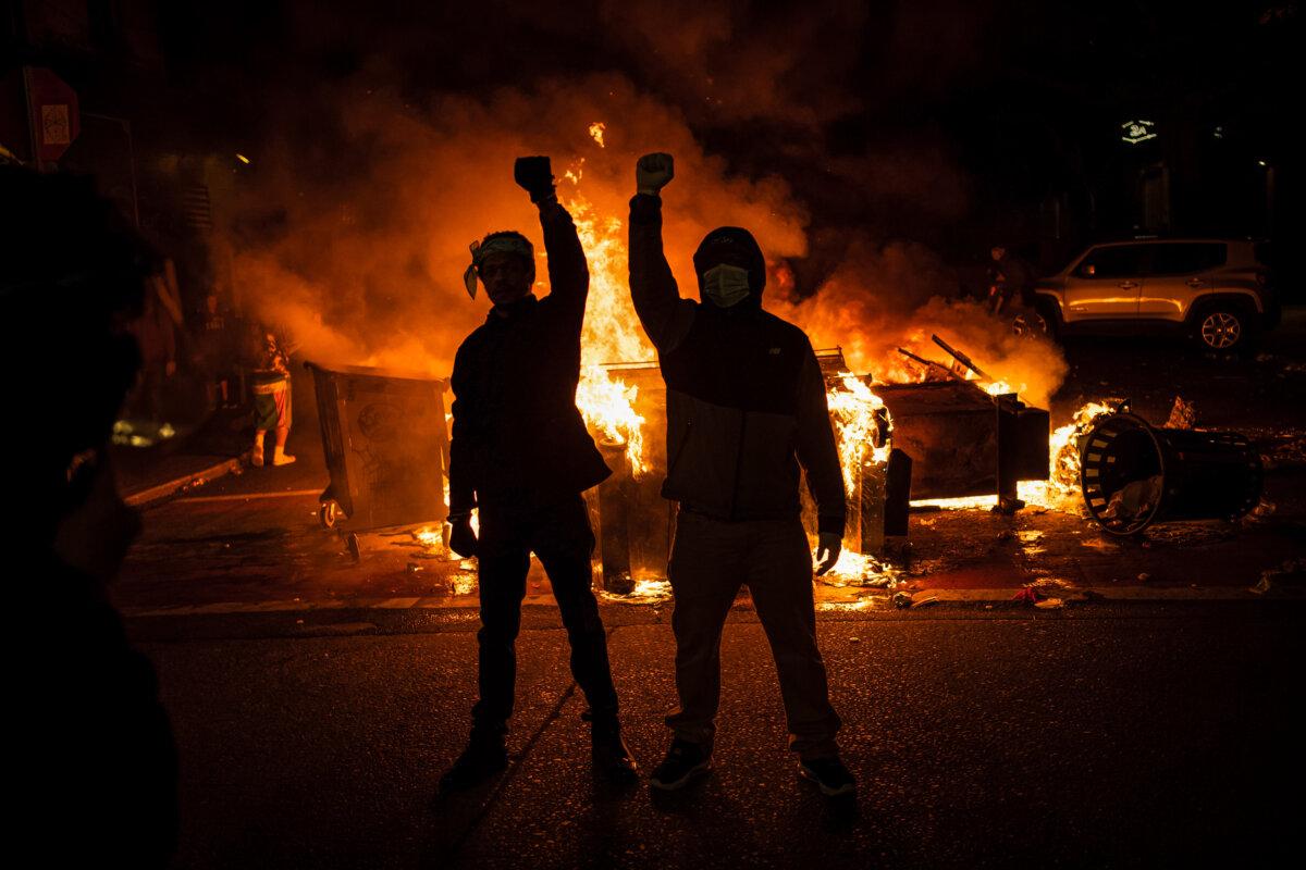 Demonstrators raise their fists as a fire burns in the street after clashes with law enforcement near the Seattle Police Department's East Precinct shortly after midnight on June 8, 2020, in Seattle, Washington, during ongoing Black Lives Matter demonstrations following the death of George Floyd. (David Ryder/Getty Images)