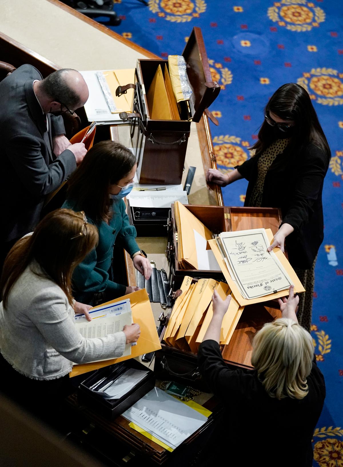  WASHINGTON, DC - JANUARY 06: Congressional aides examine electoral college votes in the House Chamber during a reconvening of a joint session of Congress on January 06, 2021 in Washington, DC. Members of Congress returned to the House Chamber after being evacuated when protesters stormed the Capitol and disrupted a joint session to ratify President-elect Joe Biden's 306-232 Electoral College win over President Donald Trump. (Photo by Drew Angerer/Getty Images)