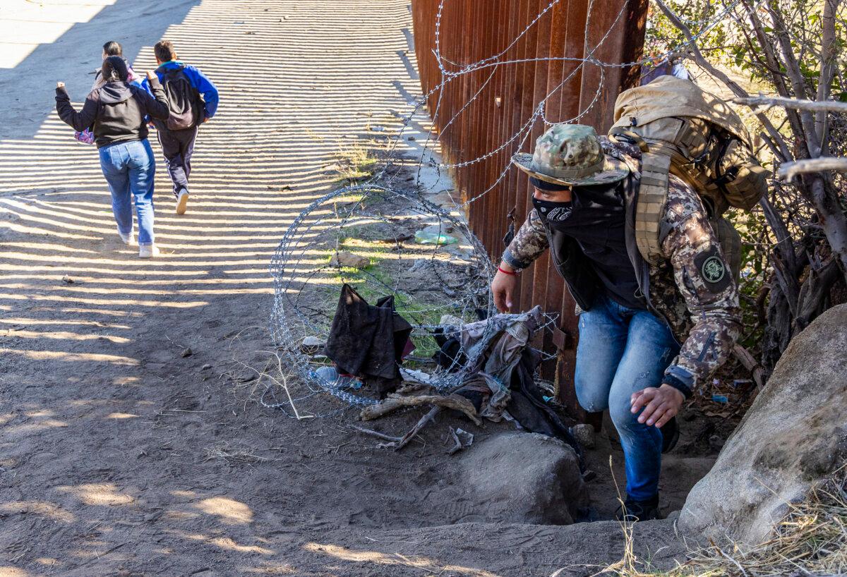 Illegal immigrants pass through a gap in the U.S. border wall to await processing by Border Patrol agents in Jacumba, Calif., on Dec. 7, 2023. (John Fredricks/The Epoch Times)