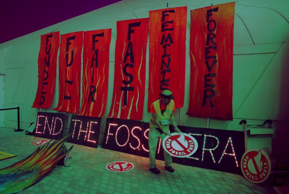 An activist places protest signs on the ground next to an illuminated sign that reads: "End the fossil era" following a protest to demand a phase out of fossil fuels on day twelve at the UNFCCC COP28 Climate Conference in Dubai on Dec. 12, 2023. (Sean Gallup/Getty Images)