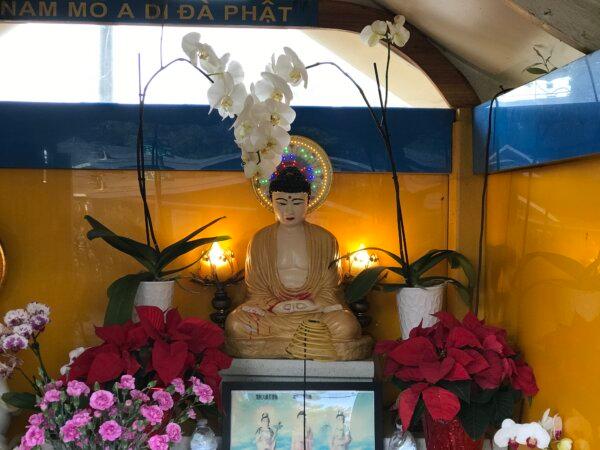 The original Buddha statue surrounded by flowers with its robe recently painted brown, on Dec. 5, 2023. (Helen Billings/The Epoch Times)