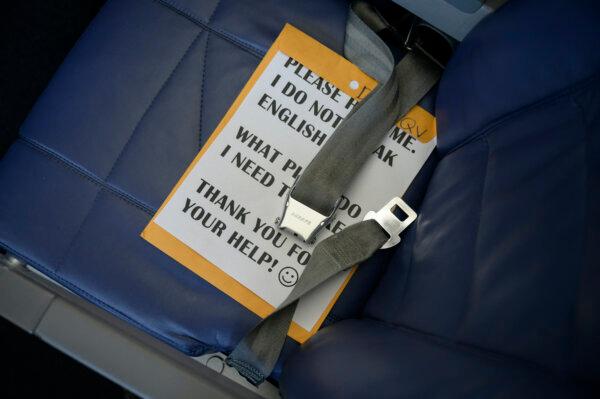 A placard asking for help with boarding a flight is displayed on a vacant seat beside Central American illegal immigrants Lidia and Isaac (unseen) aboard their flight from McAllen to Houston after being released from a U.S. government holding facility for illegal immigrants seeking asylum in McAllen, Texas, on March 30, 2021. (Ed Jones/AFP via Getty Images)