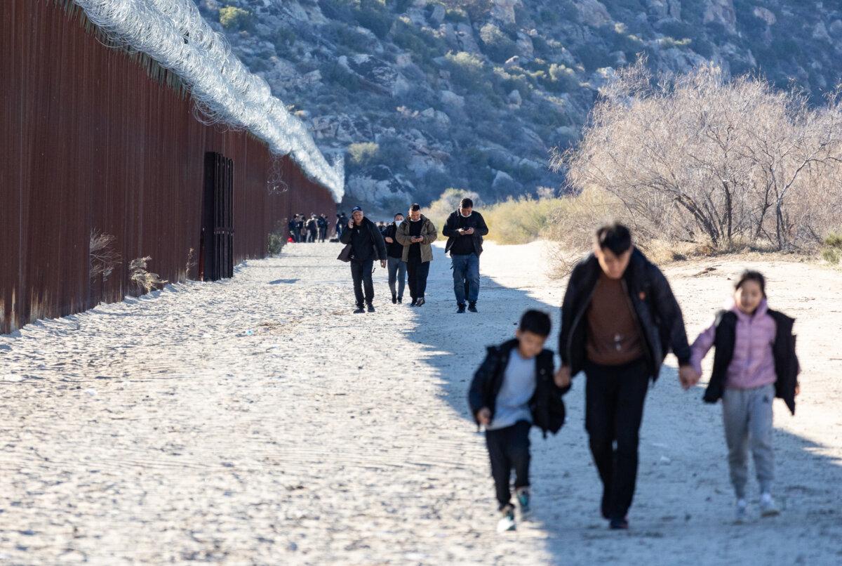 Migrants walk along the U.S. side of the United States border wall after crossing through an open gap in Jacumba, Calif., on Dec. 6, 2023. (John Fredricks/The Epoch Times)