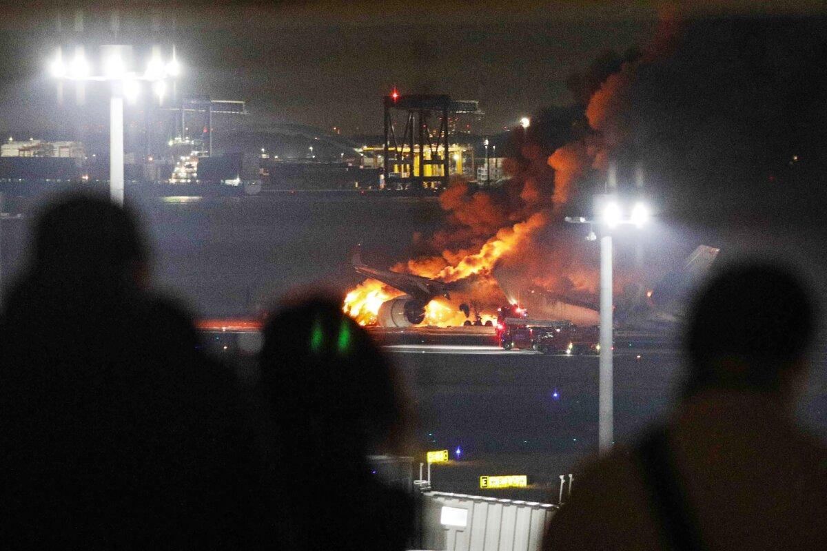 People on an observation deck looking at a Japan Airlines plane on fire on a runway of Tokyo’s Haneda Airport, on Jan. 2, 2024. (Jiji Press/AFP via Getty Images)