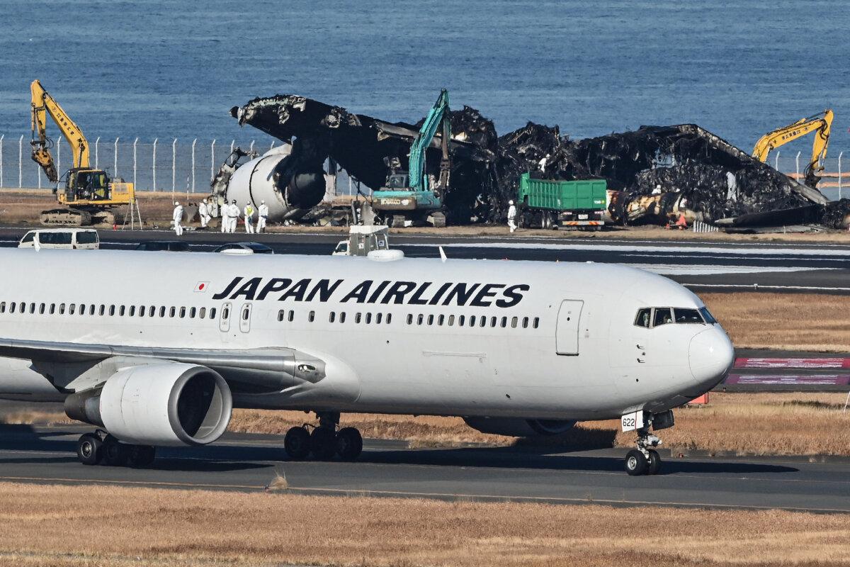 A Japan Airlines (JAL) plane taxis past the remaining debris (behind) of a JAL passenger plane from the runway area at Tokyo International Airport at Haneda on Jan. 5, 2024, three days after the JAL airliner hit a smaller coast guard plane on the ground. (Richard Brooks/AFP via Getty Images)