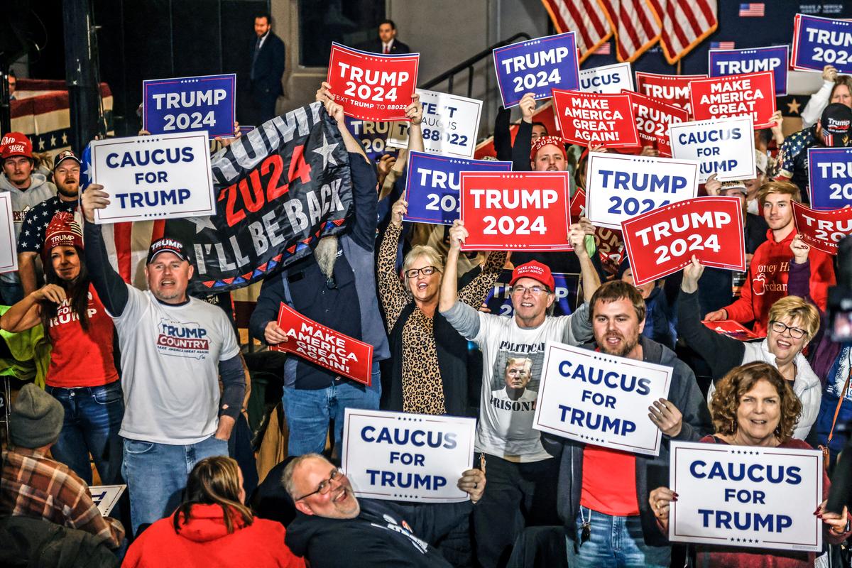 Supporters hold signs in front of TV cameras as they wait for the arrival of Republican presidential candidate Donald Trump to speak at a “Commit to Caucus” rally in Clinton, Iowa, on Jan. 6, 2024. (Tannen Maury/AFP via Getty Images)