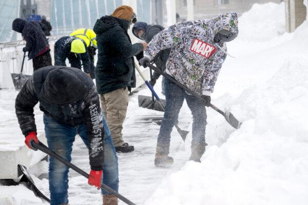 Workers clear a sidewalk of snow in Des Moines, Iowa, on January 13, 2024, as record-breaking cold continues to complicate the Iowa caucuses with snowy weather canceling many events. (Jim Watson/ AFP)