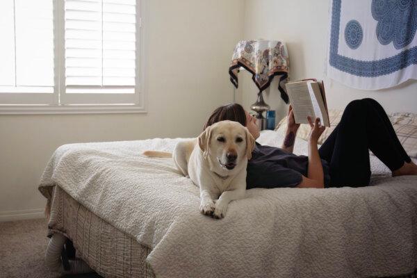 A woman rests against her dog on a bed while reading a book. (Getty Images)