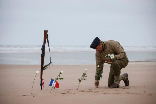 A World War II reenactor plants roses on Omaha Beach in Saint-Laurent-sur-Mer, Normandy, France, on June 6, 2023. (Thomas Padilla/AP Photo)