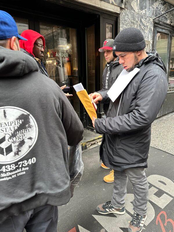 Attendants review the paperwork of newly arrived illegal immigrants in front of Vander Bar on East 45 Street in Manhattan, on Jan. 22, 2024. (Juliette Fairley)