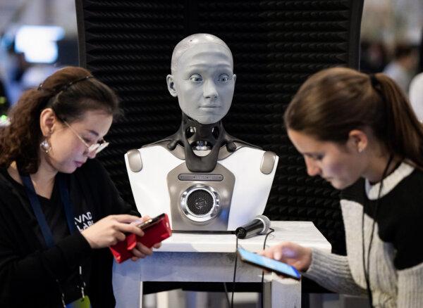 People check their phones as AMECA, an AI robot, looks on at the All In artificial intelligence conference in Montreal on Sept. 28, 2023. (Ryan Remiorz /The Canadian Press)
