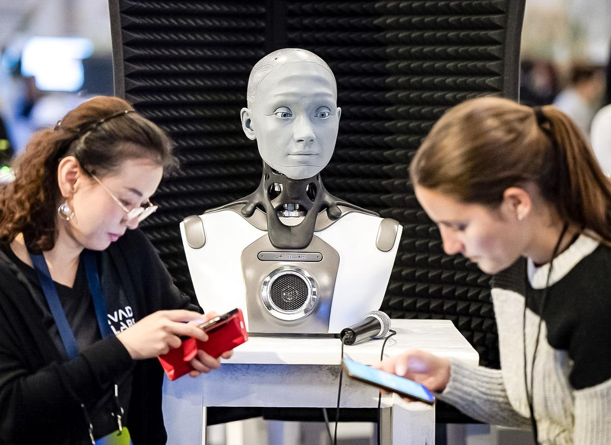 People check their phones as AMECA, an AI robot, looks on at the All In artificial intelligence conference in Montreal on Sept. 28, 2023. (Ryan Remiorz /The Canadian Press)