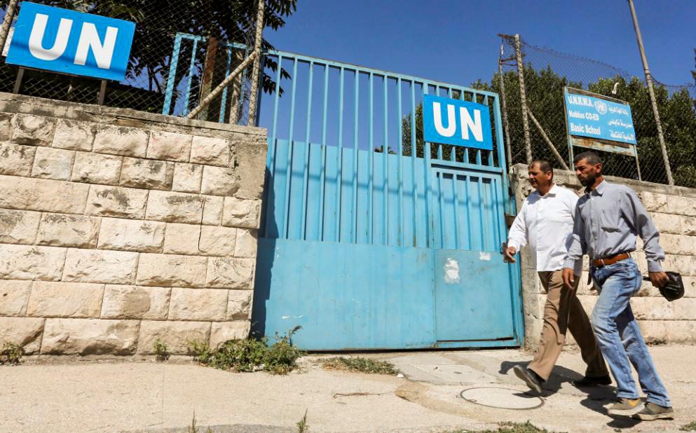 Watchdog Accuses UN Agency Staff of Stealing Gaza Humanitarian Aid, Selling It for Profit 2 Palestinians pass by the gate of an UNRWA-run school in Nablus in the West Bank, Aug. 13, 2018. (Abed Omar Qusini/Reuters)