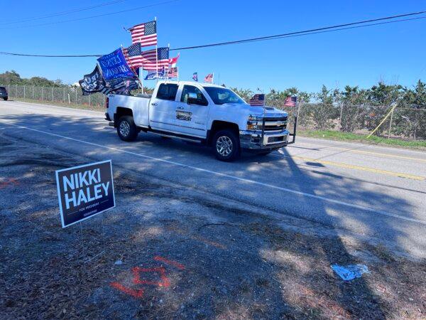 A pickup truck displaying flags including flags in support of President Donald Trump cruises past the site of a Nikki Haley campaign event in Columbia, S.C., on Feb. 1, 2024. (Lawrence Wilson/The Epoch Times)