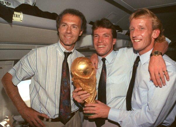 (L–R) Germany national soccer team's Franz Beckenbauer, Lothar Matthaeus, and Andreas Brehme pose with the World Cup trophy on July 9, 1990. (Wolfgang Eilmes/dpa via AP)