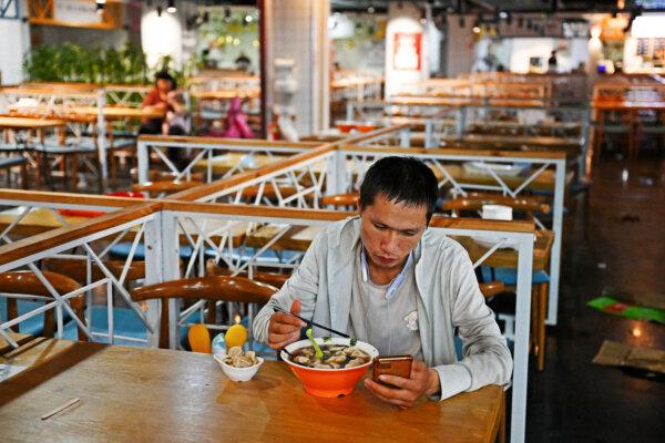 A man checks his phone while eating in a food court at a mall in Beijing on Aug. 15, 2023. (Photo by Greg Baker / AFP) (Photo by GREG BAKER/AFP via Getty Images)