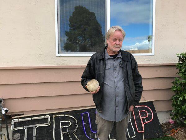 Mike Briard holding a rock that was previously thrown through a window behind him, in Martinez, Calif., on Feb. 6, 2024. (Keegan Billings/The Epoch Times)