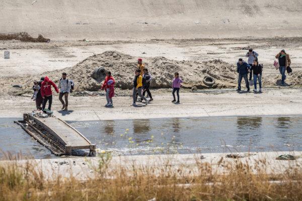 Migrants cross the Tijuana River and move toward the U.S. border wall in Tijuana, Mexico, on May 11, 2023. (John Fredricks/The Epoch Times)
