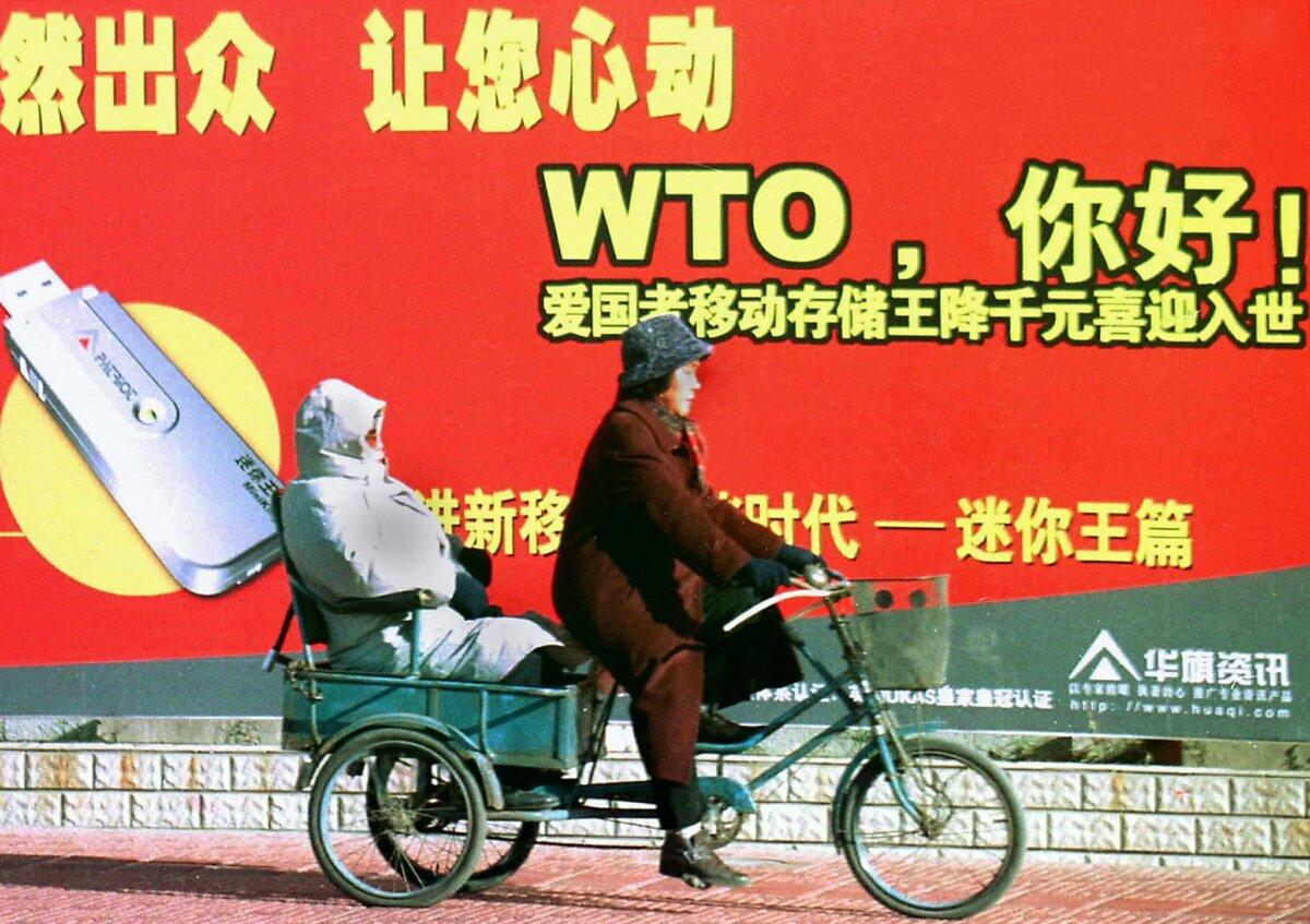 A Chinese couple on a tricycle pass a billboard welcoming the country's membership to the World Trade Organization (WTO), along a street in Beijing on Dec. 23, 2001. (AFP via Getty Images)
