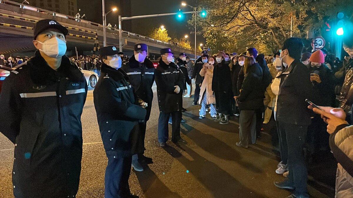 Policemen watch over protesters gathering along a street during a rally for the victims of a deadly fire as well as a protest against China's harsh COVID-19 restrictions in Beijing on Nov. 28, 2022. (Michael Zhang/AFP via Getty Images)