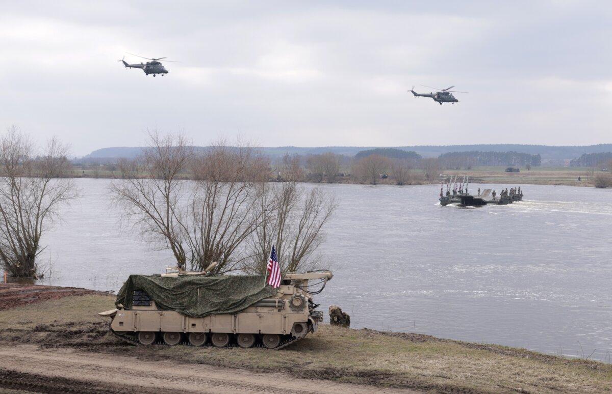 Polish army helicopters fly over the Vistula River as a U.S. combat vehicle passes during NATO's Dragon 24 military exercise near Gniew, Poland, on March 4, 2024. (Sean Gallup/Getty Images)